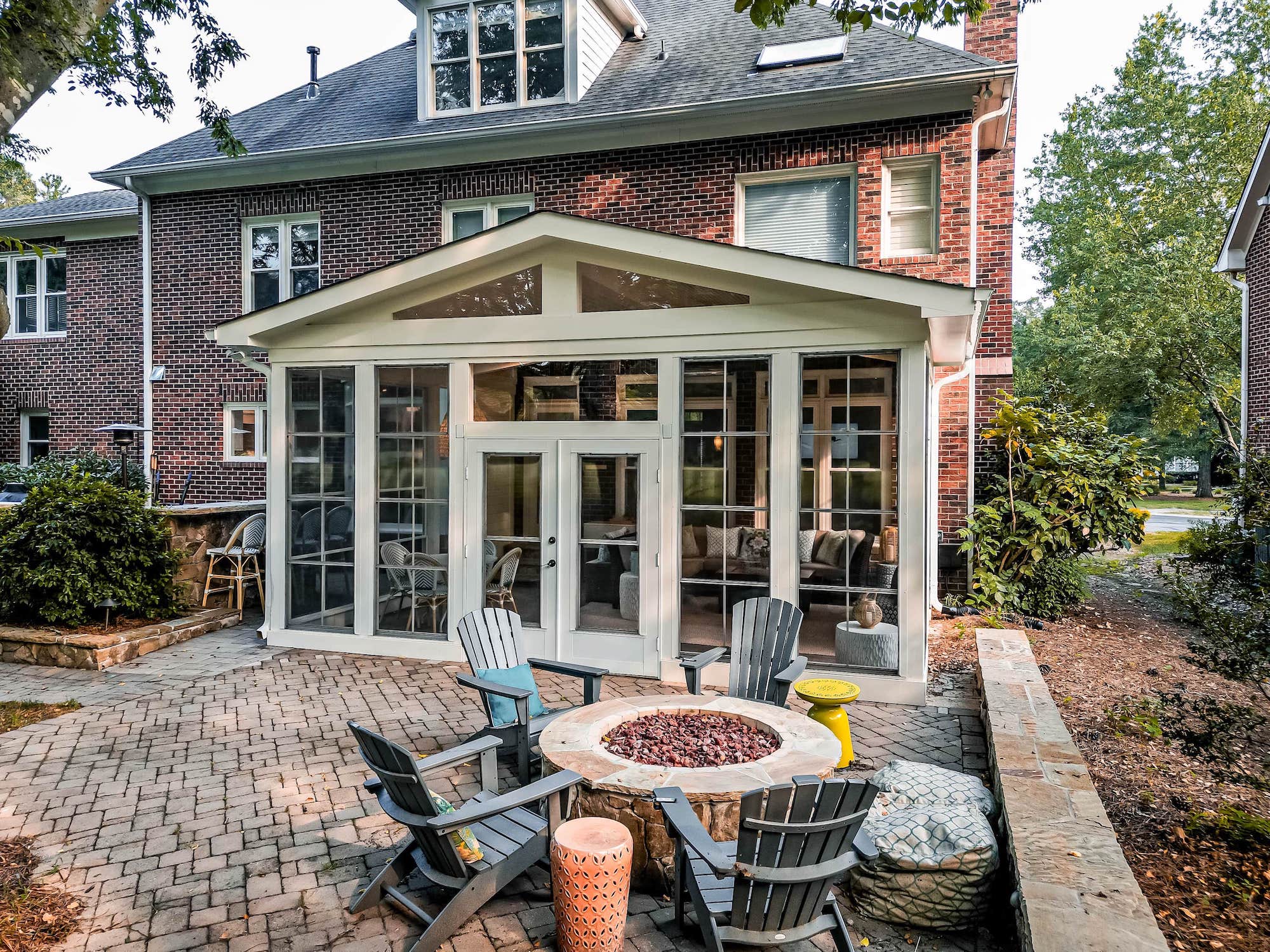 Gabled white sunroom and herringbone paver patio with a stone gas fire pit, custom built by Carolina Decks in the Charlotte, NC area.