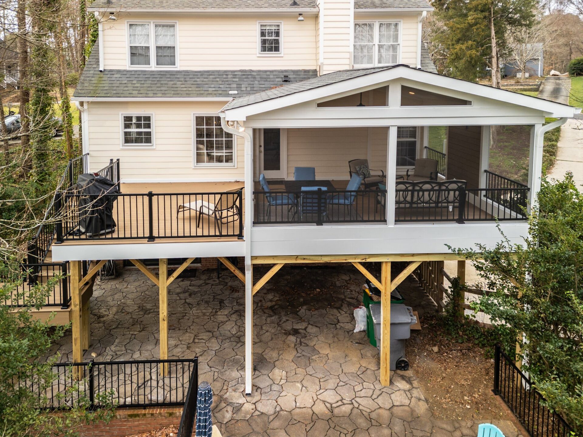 An elevated composite deck, gable roof screened porch with black railings, and a stone patio below, custom built by Carolina Decks in South Charlotte