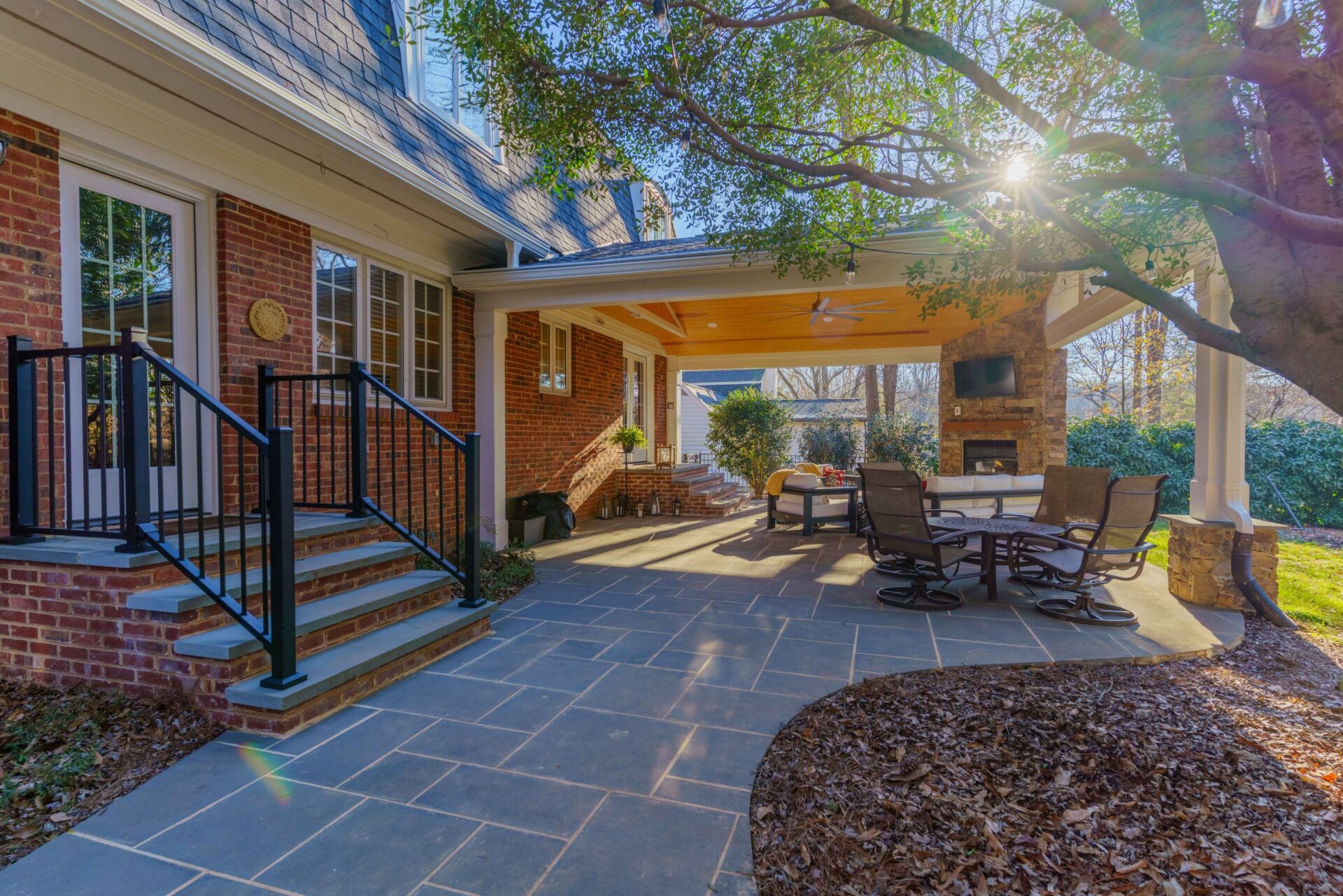 Covered bluestone patio, stone fireplace with TV, and warm wood ceiling with fan, custom built by Carolina Decks in the Charlotte, NC area.