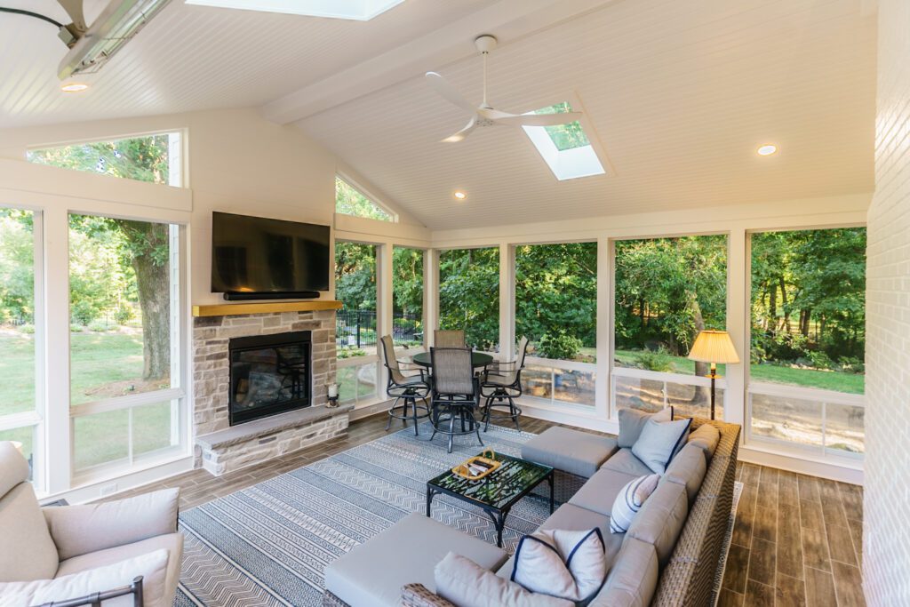 An elegant enclosed porch features a stone fireplace, vaulted ceiling, large windows, and skylights, custom built by Carolina Decks in the Charlotte, NC area.