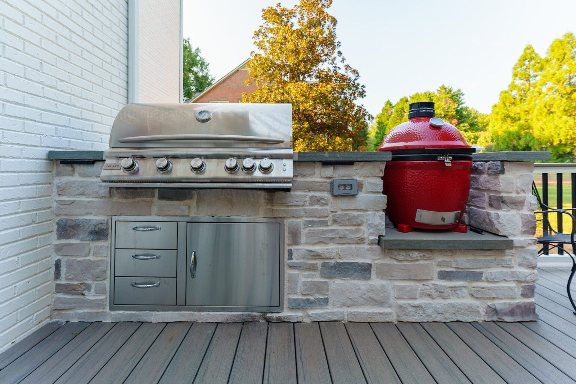 A modern outdoor kitchen with stone veneer, built-in stainless grill, Kamado Joe smoker, and composite deck, custom built by Carolina Decks in the Chadwyck Farms neighborhood.