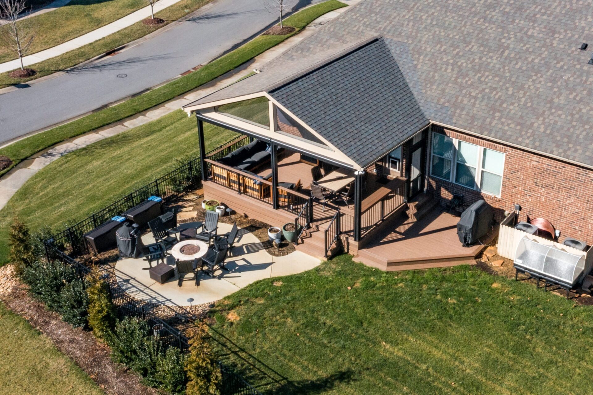 Expansive composite deck with a gabled roof, black railings, and a concrete patio with fire pit, custom built by Carolina Decks in the Davidson area.