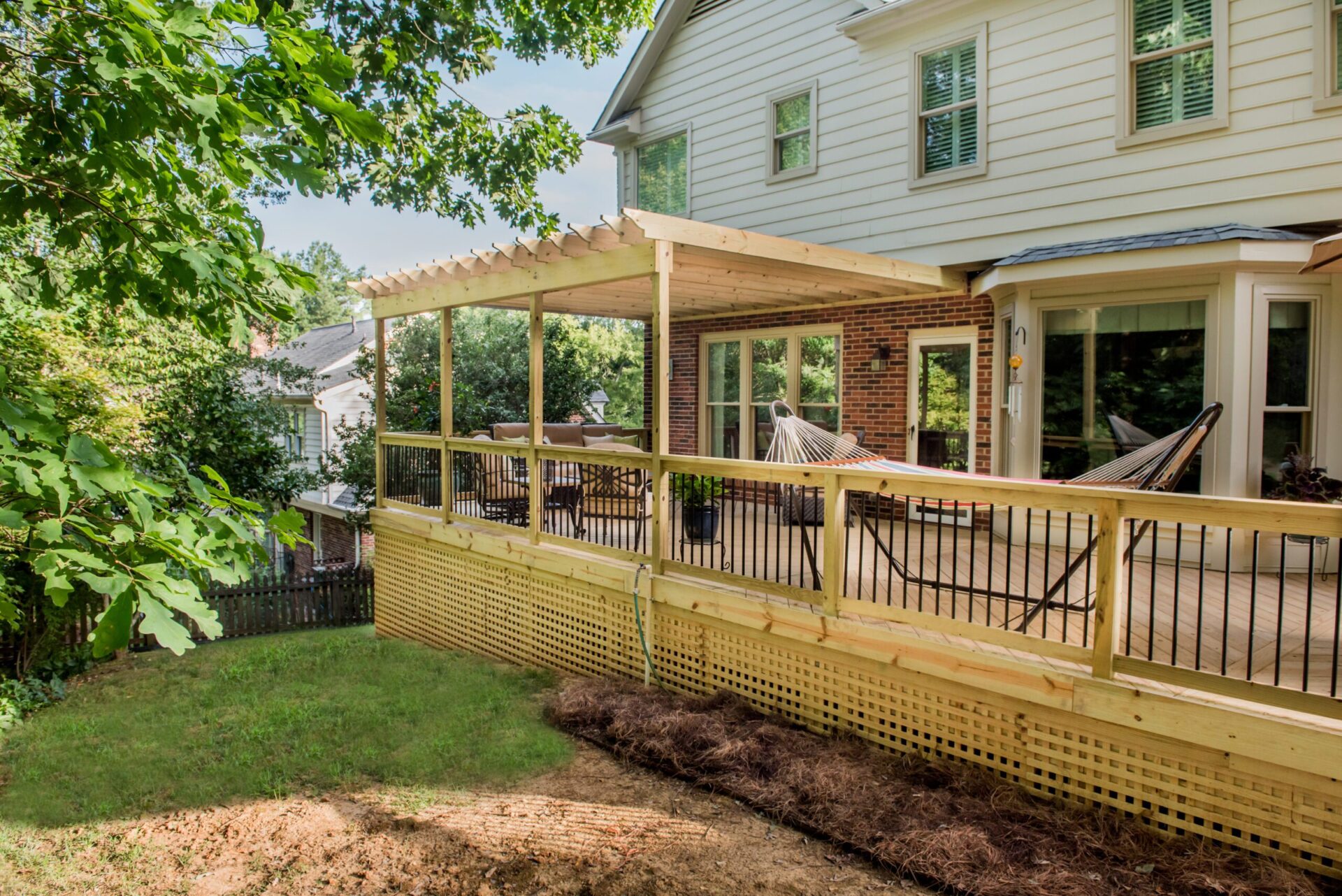 Expansive wooden deck with an attached covered pergola, lattice skirting, and black balusters custom built by Carolina Decks in the Fort Mill, SC area.