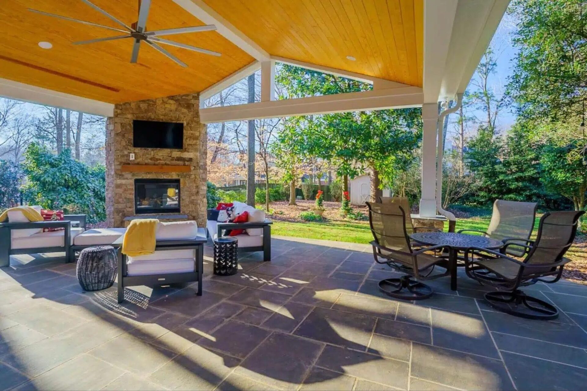 Expansive covered patio with stone fireplace, wood plank ceiling, and paver floor, custom built by Carolina Decks in the Charlotte, NC area.