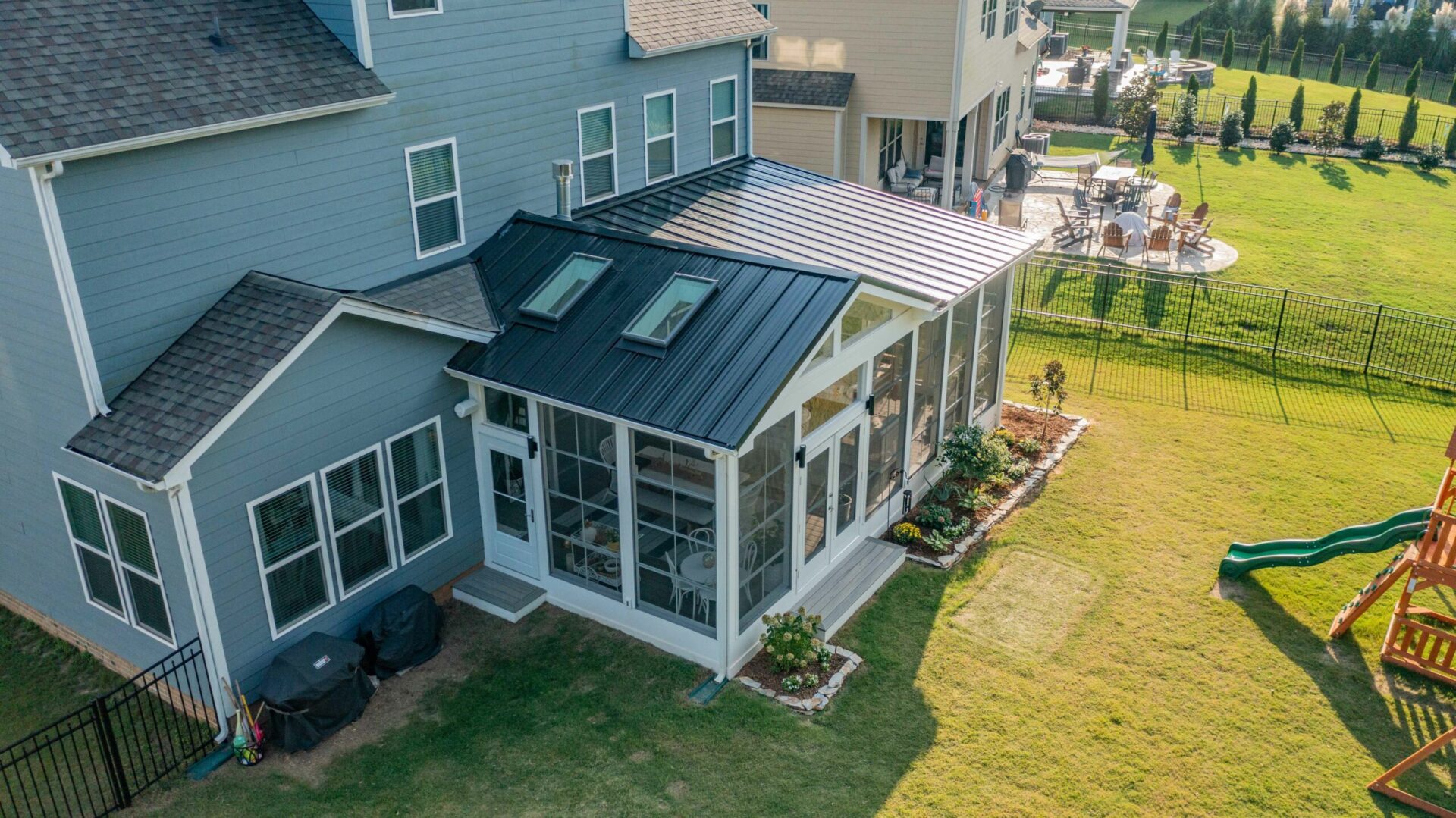 Aerial view of a custom screen porch addition on a blue siding home in the Millbridge neighborhood of Waxhaw, NC. The porch features a black standing seam metal roof, integrated skylights, white trim, and double doors opening to the backyard.