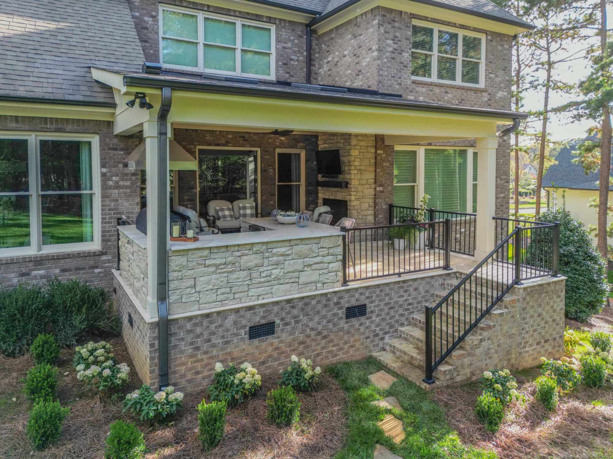 Covered stone patio with outdoor fireplace, brick stairs, and black railings, custom built by Carolina Decks in the Charlotte, NC area.