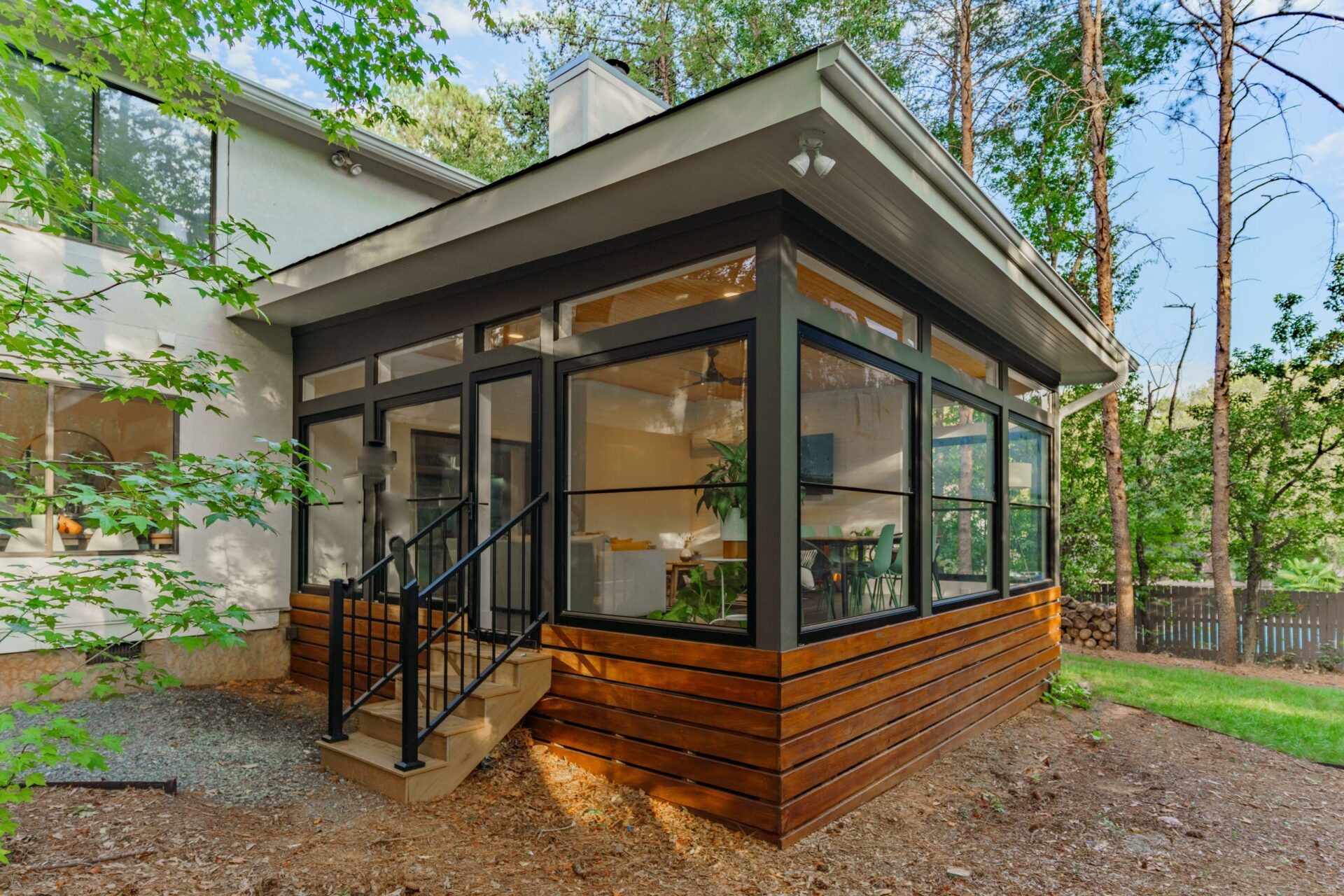Modern glass sunroom with wood siding, black railings, and steps, custom built by Carolina Decks in the Charlotte, NC area.