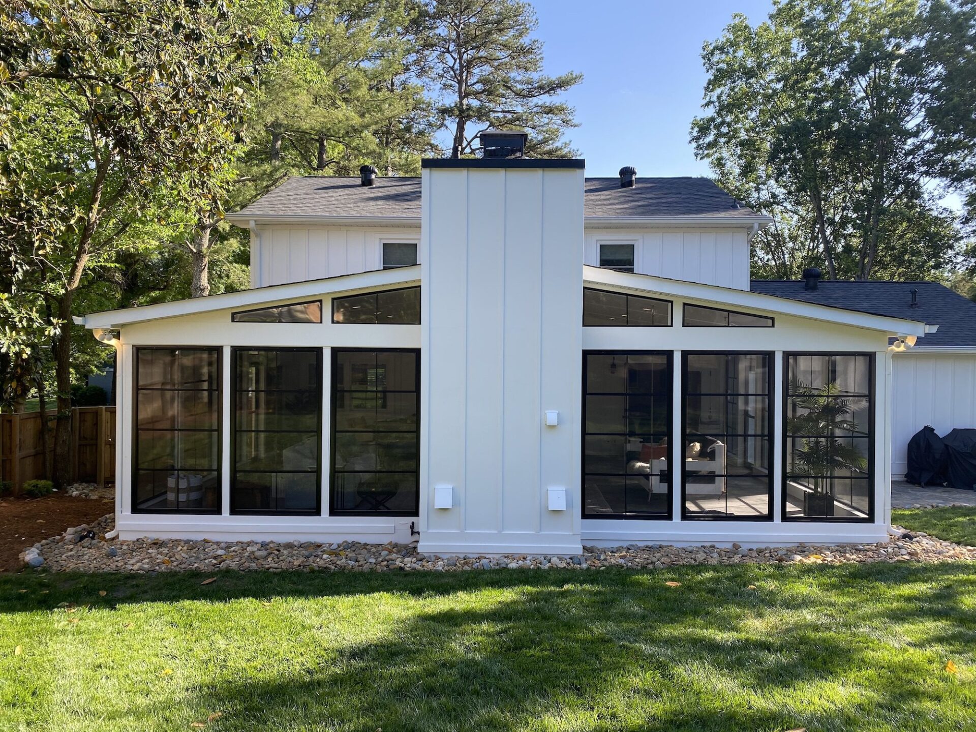 Symmetrical exterior shot of a modern white screened porch addition with black-framed Eze-Breeze windows and a central chimney in Lynbrook, Charlotte.