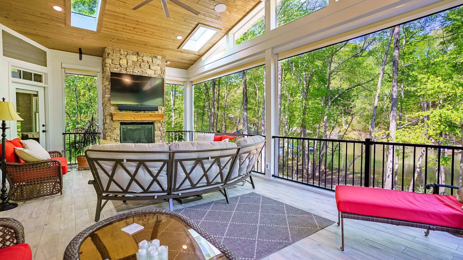 Interior view of a luxury screened porch featuring a large floor-to-ceiling brick fireplace with a wood mantle, a mounted TV, and a stained wood ceiling near Lake Norman.