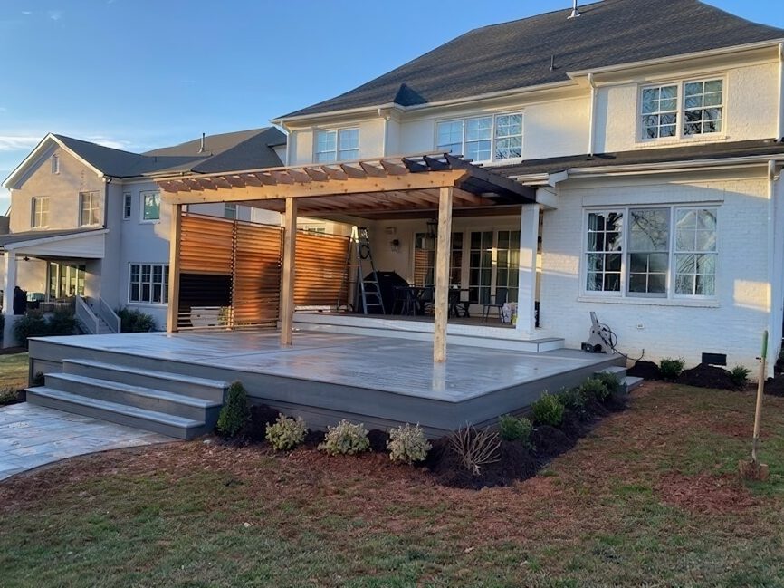 Spacious grey composite deck, natural wood pergola, and horizontal slat privacy wall, custom built by Carolina Decks in the Charlotte, NC area.