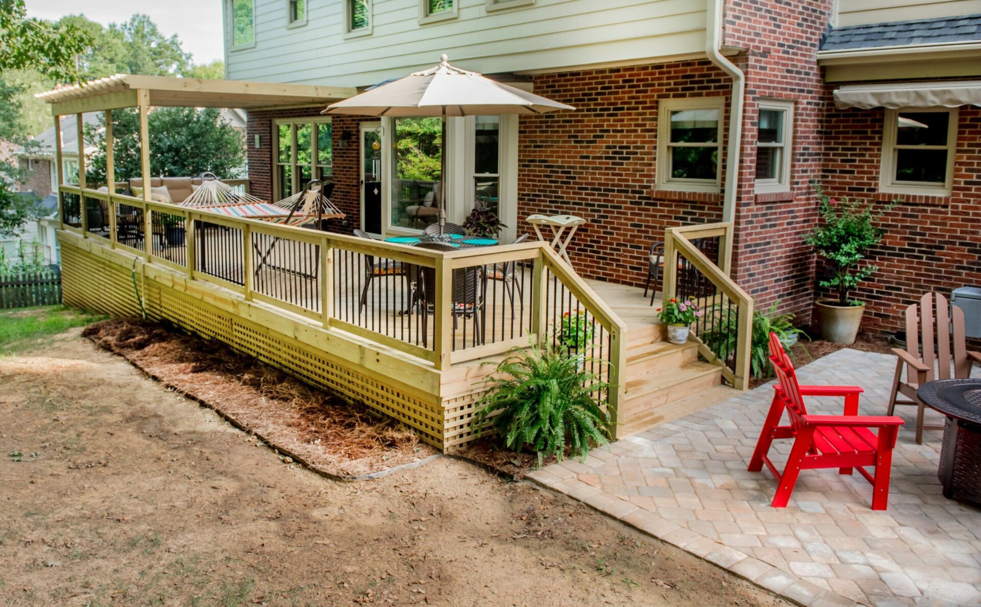 Elevated wood deck with attached pergola, black baluster railing, and paver patio, custom built by Carolina Decks in the South Charlotte, NC area.