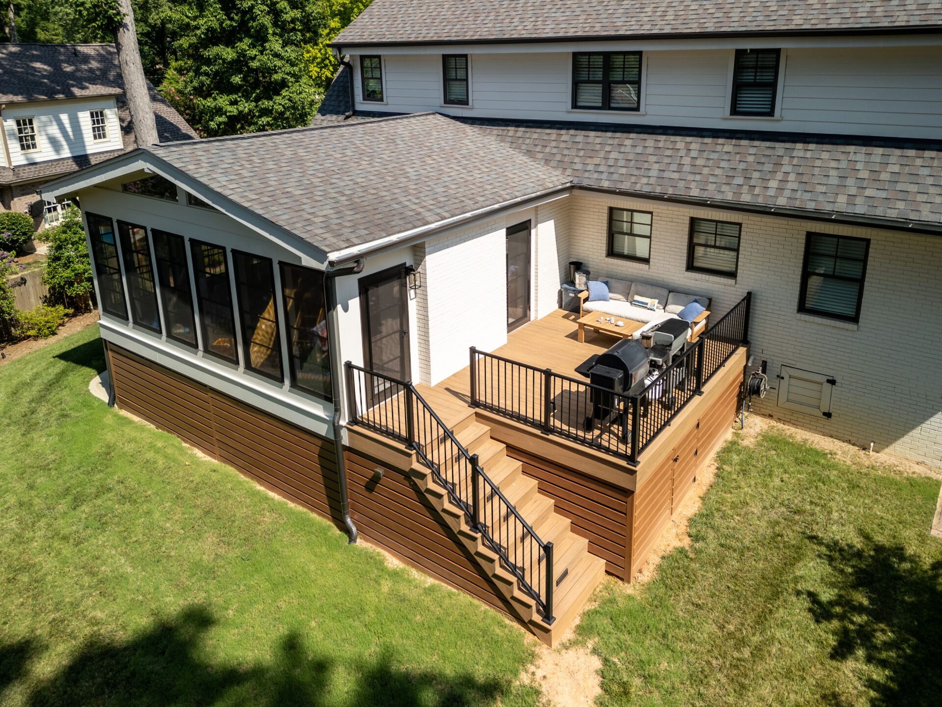Elevated light composite deck with black railings and steps to an enclosed porch, custom built by Carolina Decks in the Charlotte, NC area.
