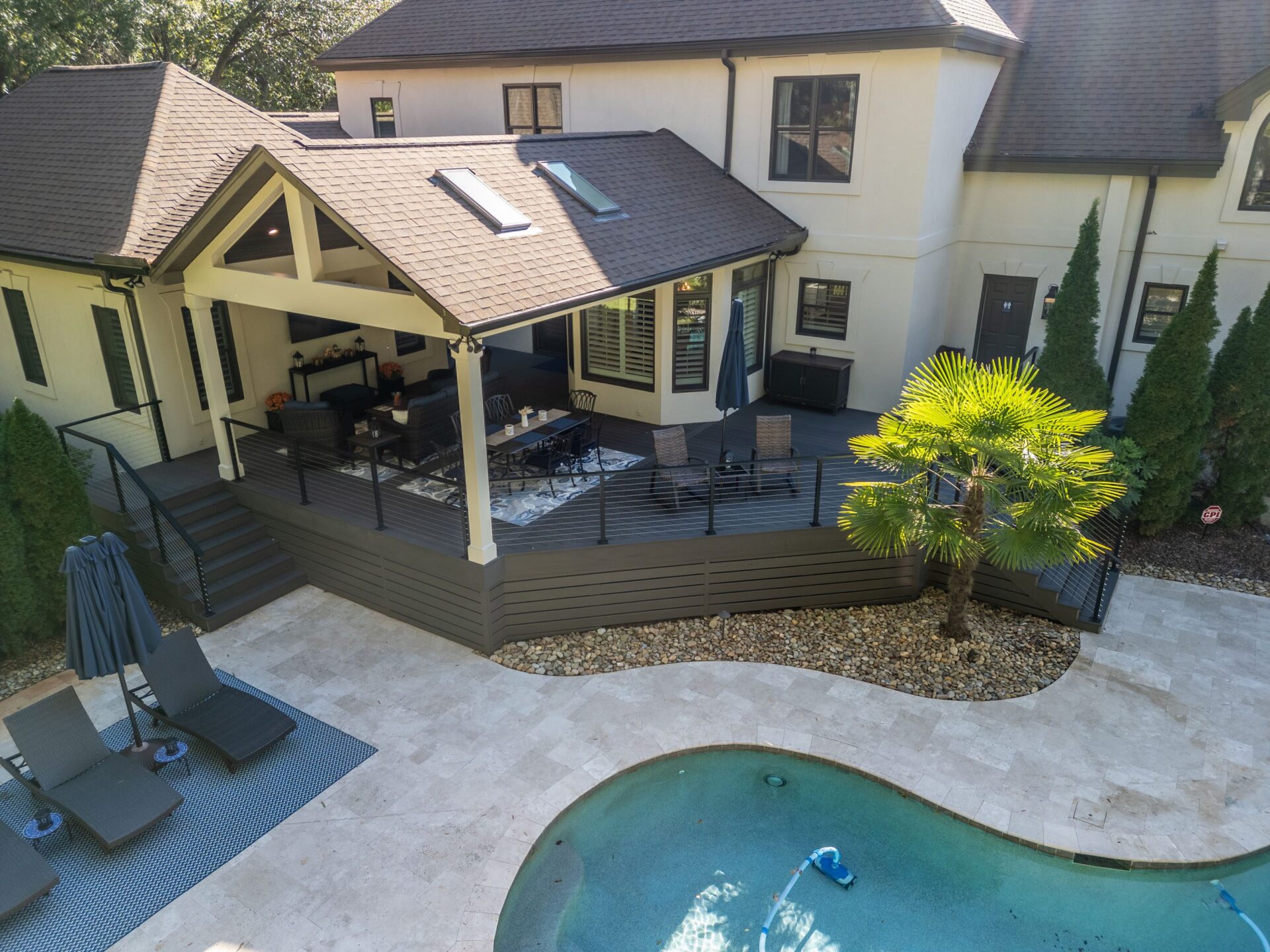 Spacious covered composite deck with cable railing, stairs, and a paver patio next to a pool, custom built by Carolina Decks in the Providence Country Club neighborhood.