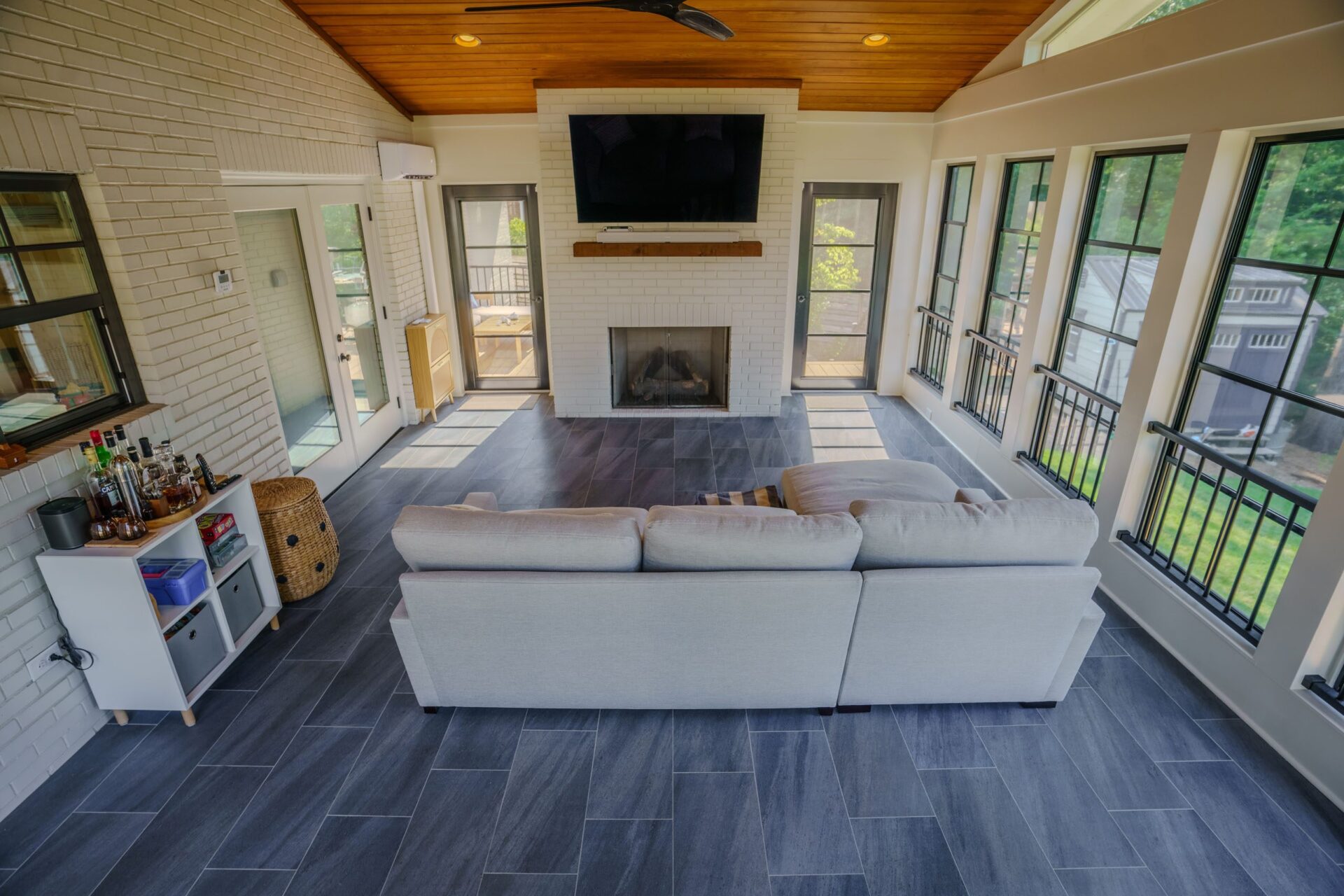 Spacious sunroom with white brick walls, wood ceiling, dark tile floor, and a fireplace, custom built by Carolina Decks in the Charlotte, NC area.