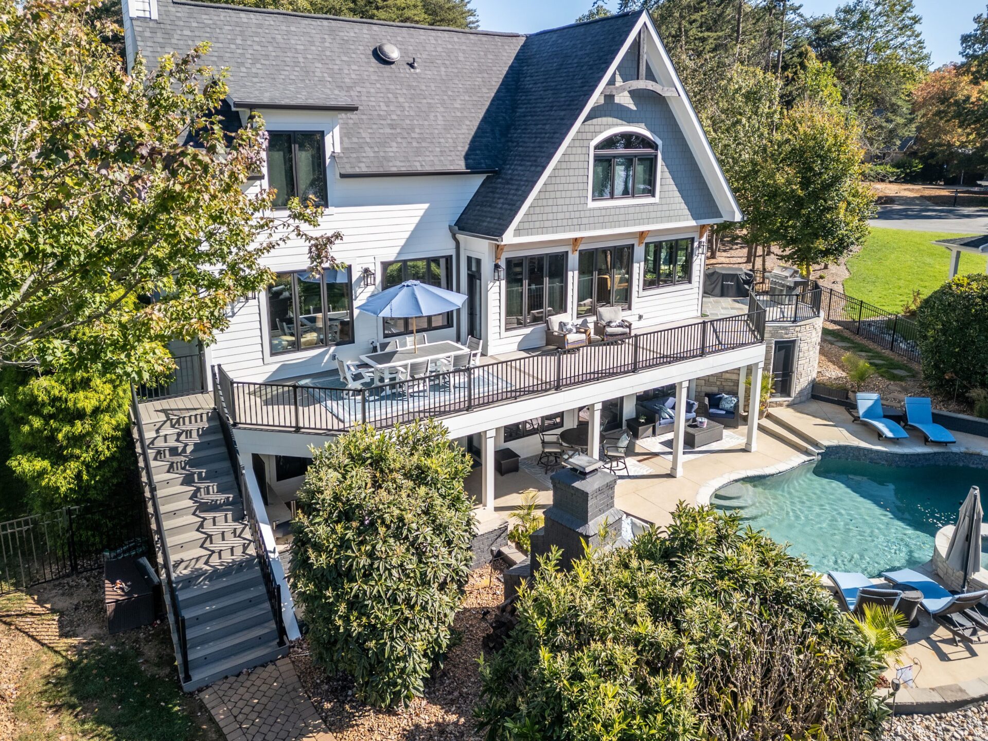 Spacious tiered composite deck with dark steps, black railings, lower patio, and swimming pool, custom built by Carolina Decks in the Charlotte, NC area.