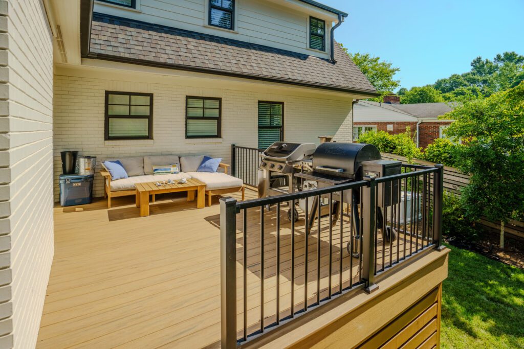 Spacious composite deck with black metal baluster railing, outdoor furniture, and grilling area, custom built by Carolina Decks in the Charlotte, NC area.