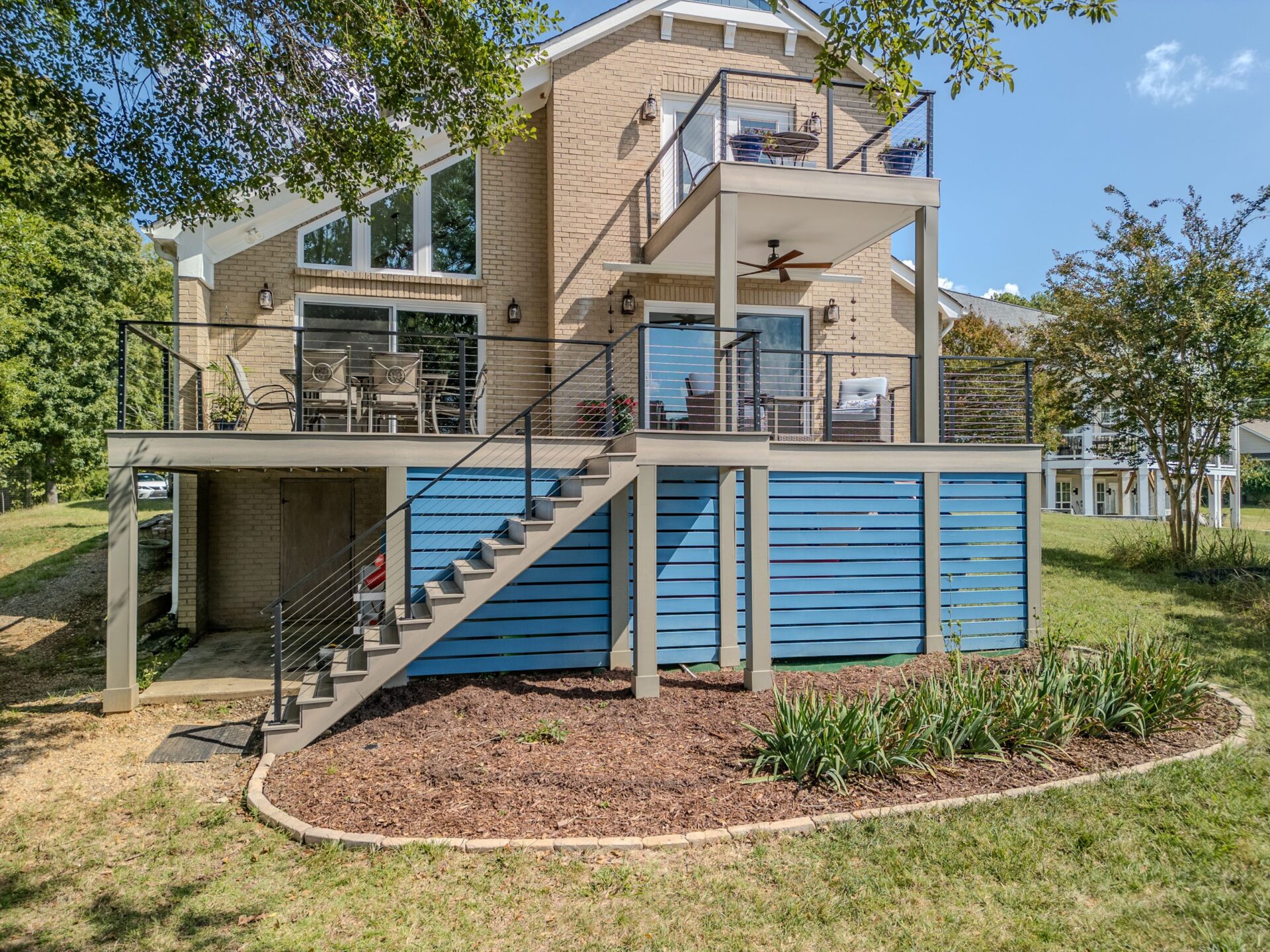 A multi-level composite deck features black cable railings, connecting stairs, and a bright blue slatted privacy screen, custom built by Carolina Decks in Tega Cay.