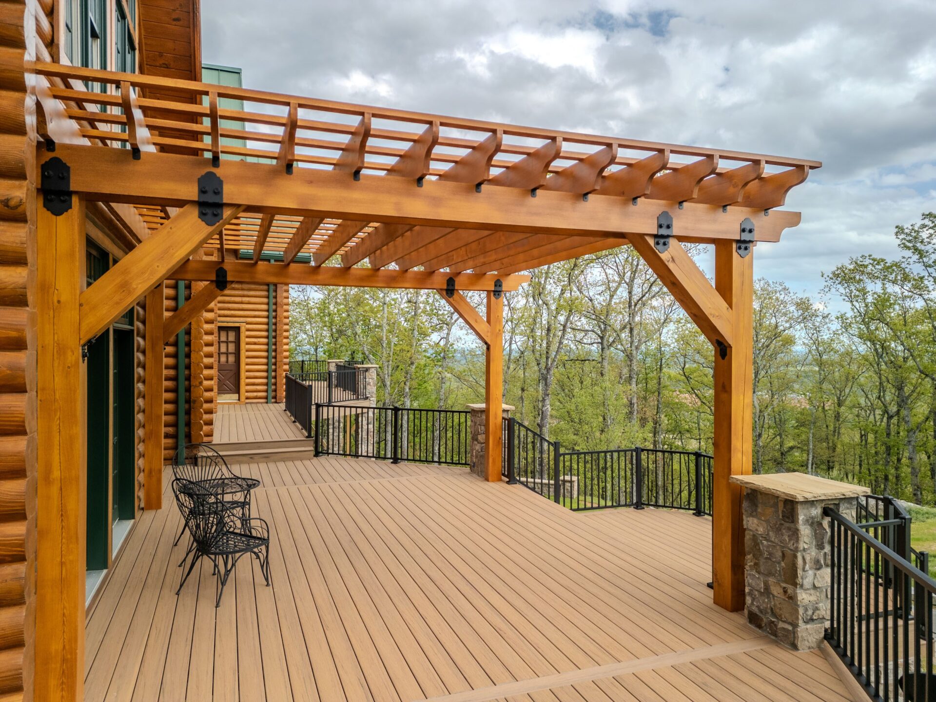 A beautiful multi-level composite deck with a custom timber pergola, black metal railings, and stone pillars, custom built by Carolina Decks in the Charlotte, NC area.