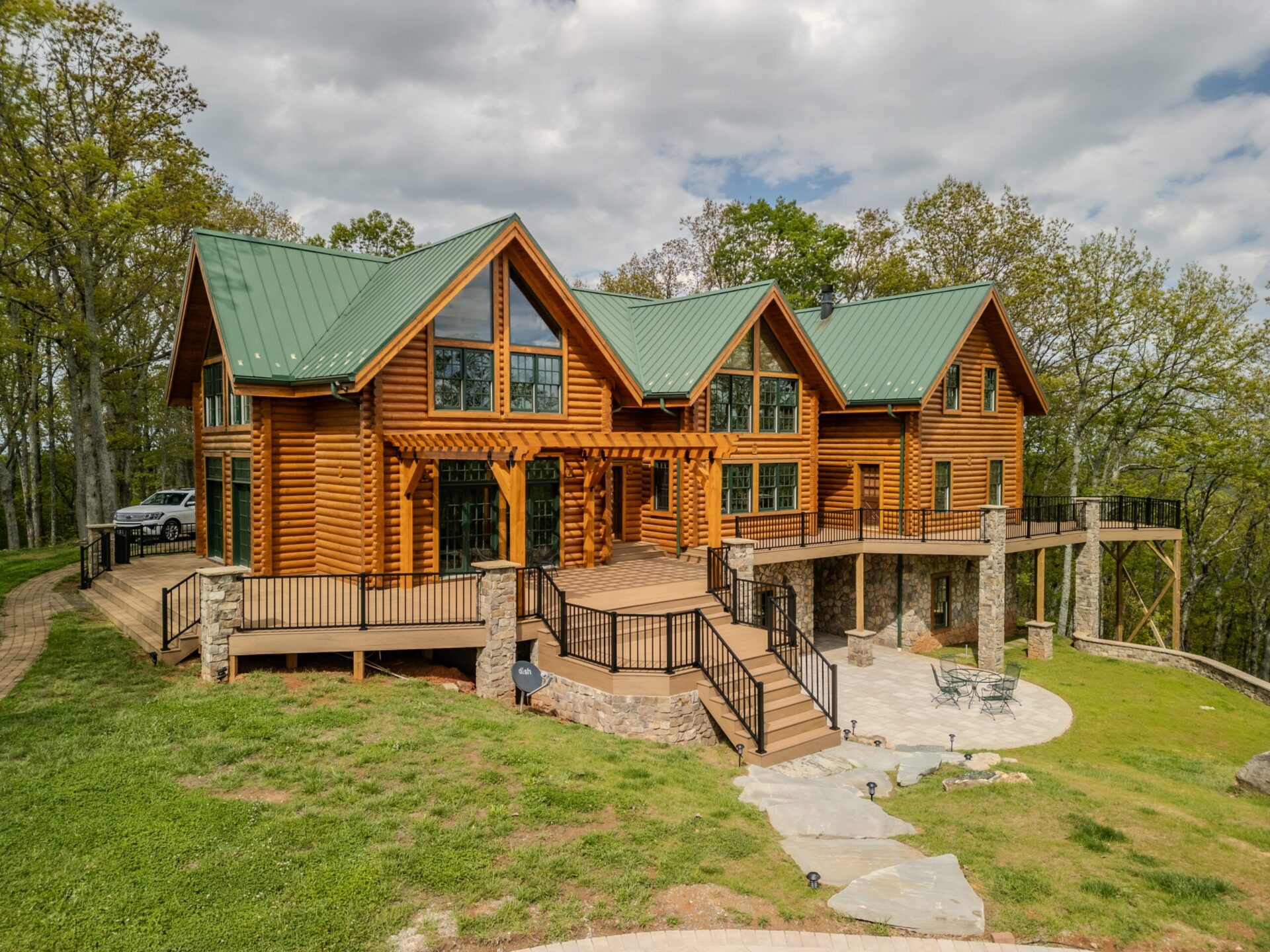 Multi-level composite deck with black railings, a wood pergola, and stone paver patio at a log home, custom built by Carolina Decks in the Charlotte, NC area.
