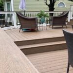 Overhead view of a composite deck in Ravencrest layout featuring brown wicker furniture, bright blue and green accent end tables, and a covered grill.