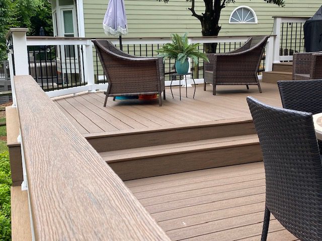 Overhead view of a composite deck in Ravencrest layout featuring brown wicker furniture, bright blue and green accent end tables, and a covered grill.
