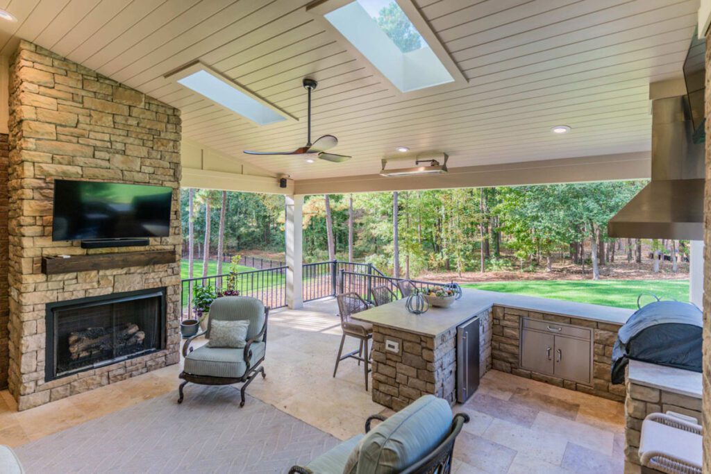 Covered patio with stone fireplace, outdoor kitchen, and travertine flooring, custom built by Carolina Decks in the Cheval neighborhood