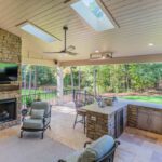 Covered patio with stone fireplace, outdoor kitchen, and travertine flooring, custom built by Carolina Decks in the Cheval neighborhood