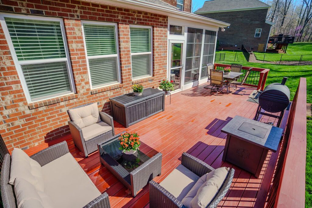 A vibrant red-stained wood deck seamlessly connects to a bright screened porch, perfect for outdoor living, custom built by Carolina Decks in the Deerbridge neighborhood.
