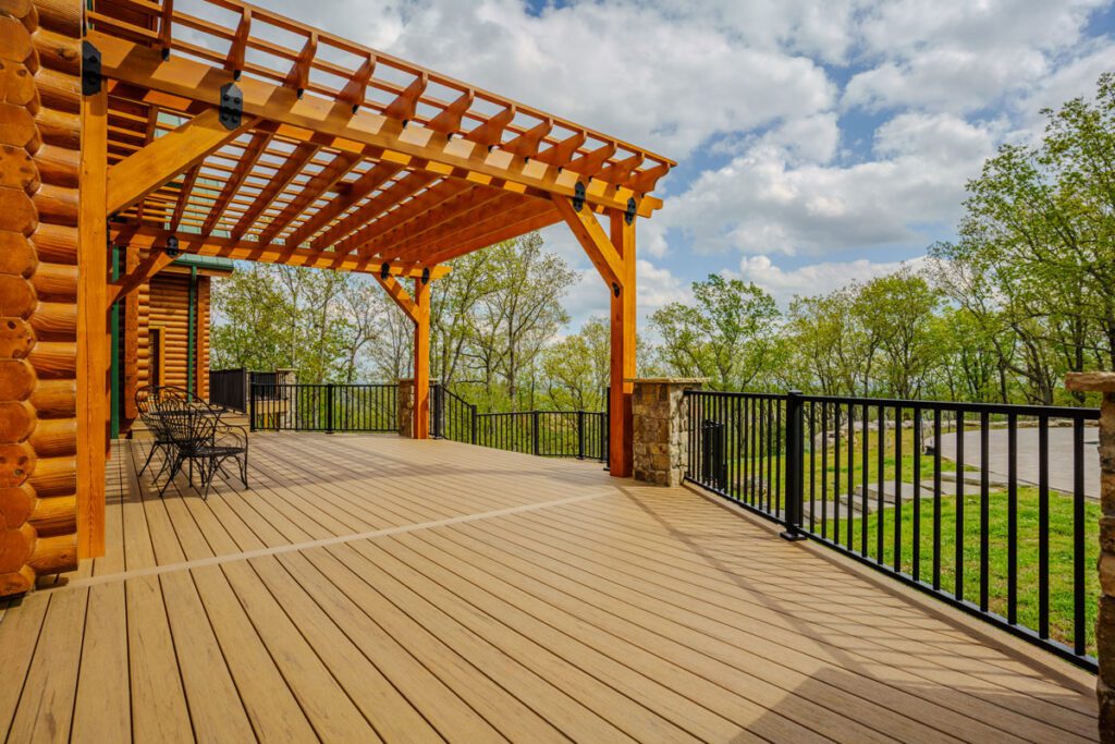 Large tan composite deck with a custom timber pergola, black metal railings, and stone posts, custom built by Carolina Decks in the Lake Norman, NC area.