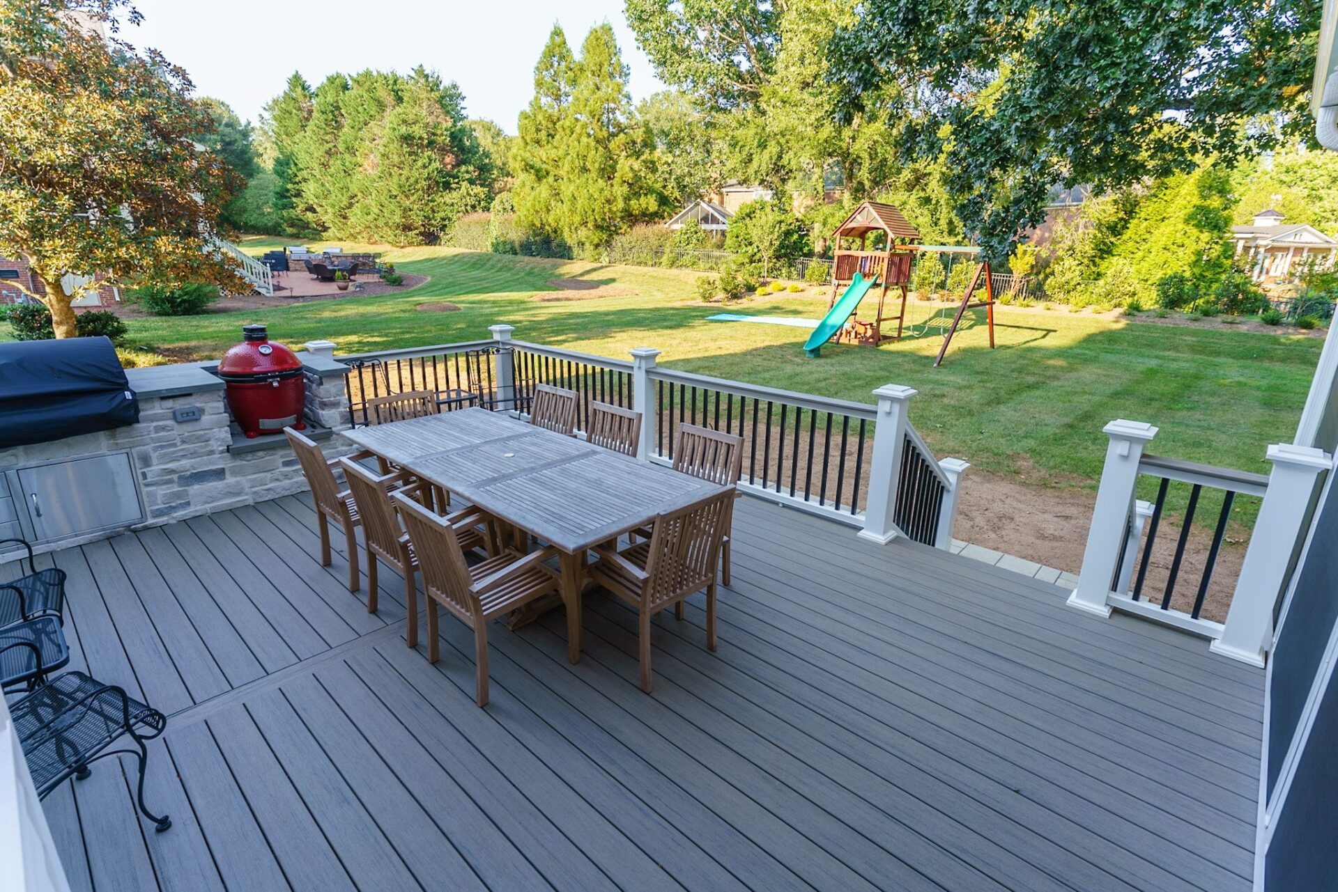 A spacious grey composite deck with a stone outdoor kitchen and modern railing system, custom built by Carolina Decks in the Charlotte, NC area.