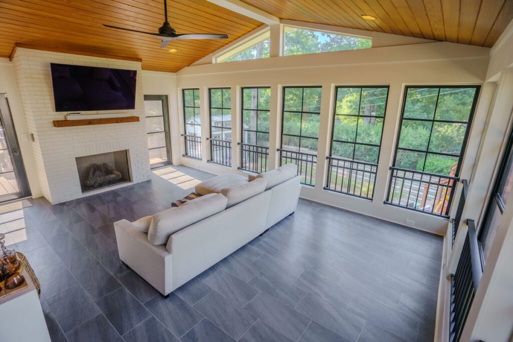 Four-season room with vaulted wood ceiling, black windows, white brick fireplace, and tile floor, custom built by Carolina Decks in the Meyers Park, NC area.