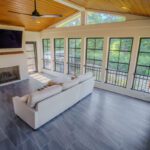 Four-season room with vaulted wood ceiling, black windows, white brick fireplace, and tile floor, custom built by Carolina Decks in the Meyers Park, NC area.