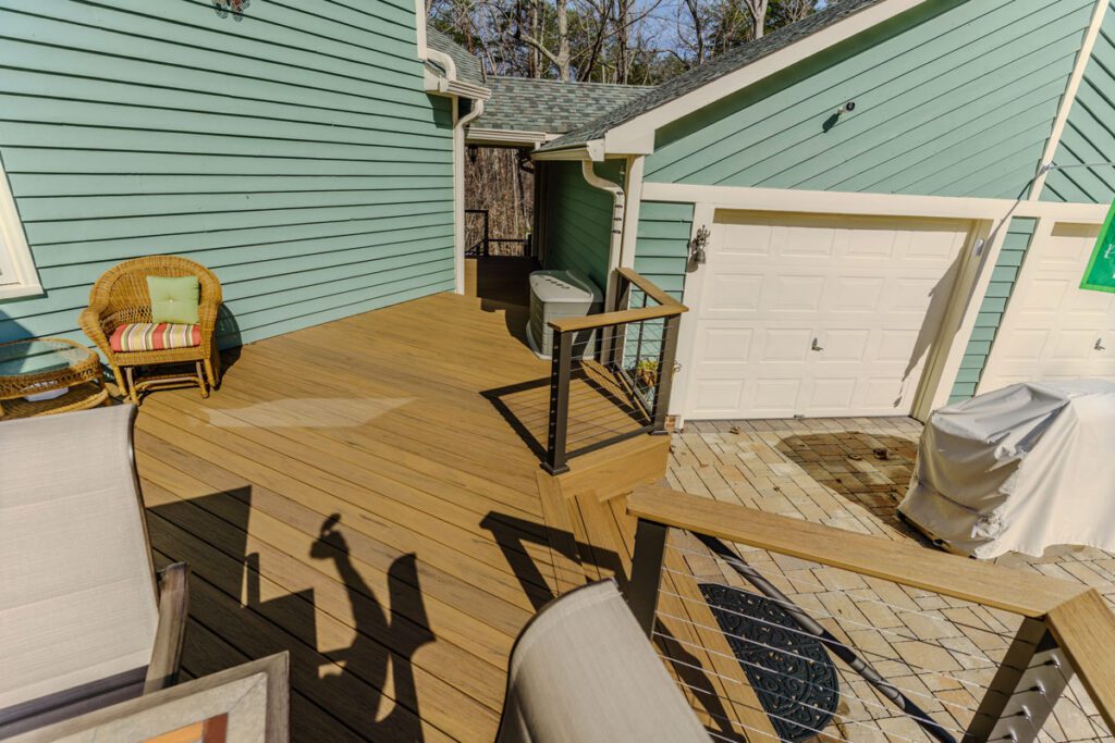 Modern light brown composite deck featuring sleek cable railing and adjacent paver patio, custom built by Carolina Decks in the Belmont, NC area.