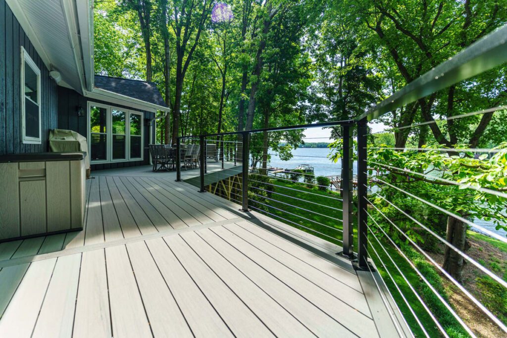 Spacious light gray composite deck with modern black cable railing overlooking a lake, custom built by Carolina Decks in the Mill Road, NC area.