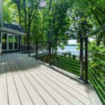 Spacious light gray composite deck with modern black cable railing overlooking a lake, custom built by Carolina Decks in the Mill Road, NC area.