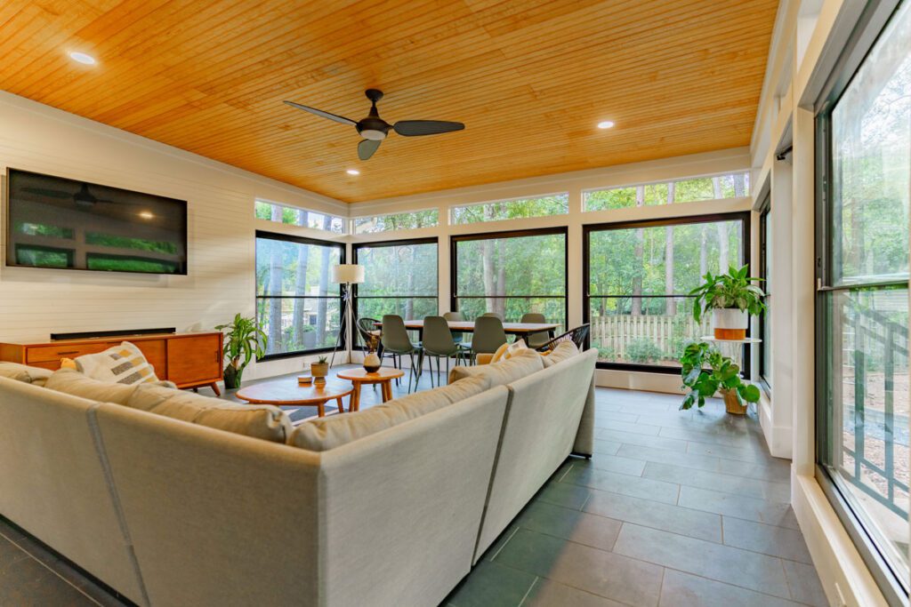 Modern sunroom with wide black windows, wood ceiling, and dark tile floor, custom built by Carolina Decks in the Rhone, NC area.