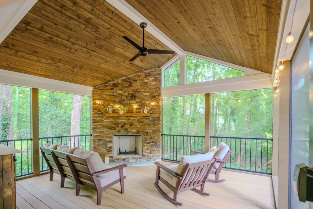 Spacious screened porch with vaulted wood ceiling, stone fireplace, light composite deck, and metal railings, custom built by Carolina Decks in the Sedgefield neighborhood.