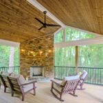 Spacious screened porch with vaulted wood ceiling, stone fireplace, light composite deck, and metal railings, custom built by Carolina Decks in the Sedgefield neighborhood.