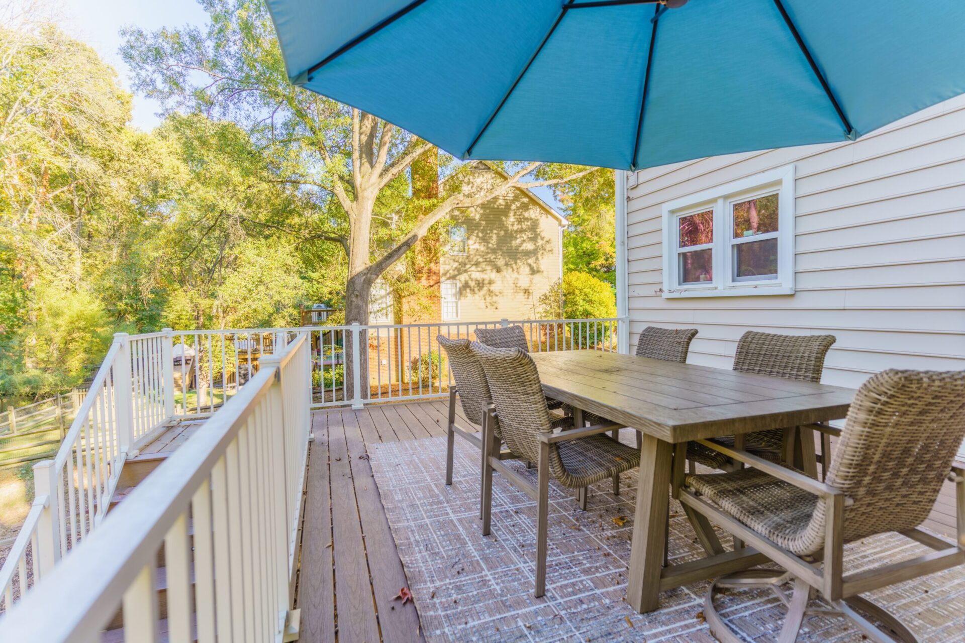 Luxury composite deck in Charlotte's Carmel neighborhood featuring a Trex white aluminum railing, a spacious outdoor dining table set under a blue umbrella, and a patterned outdoor area rug.
