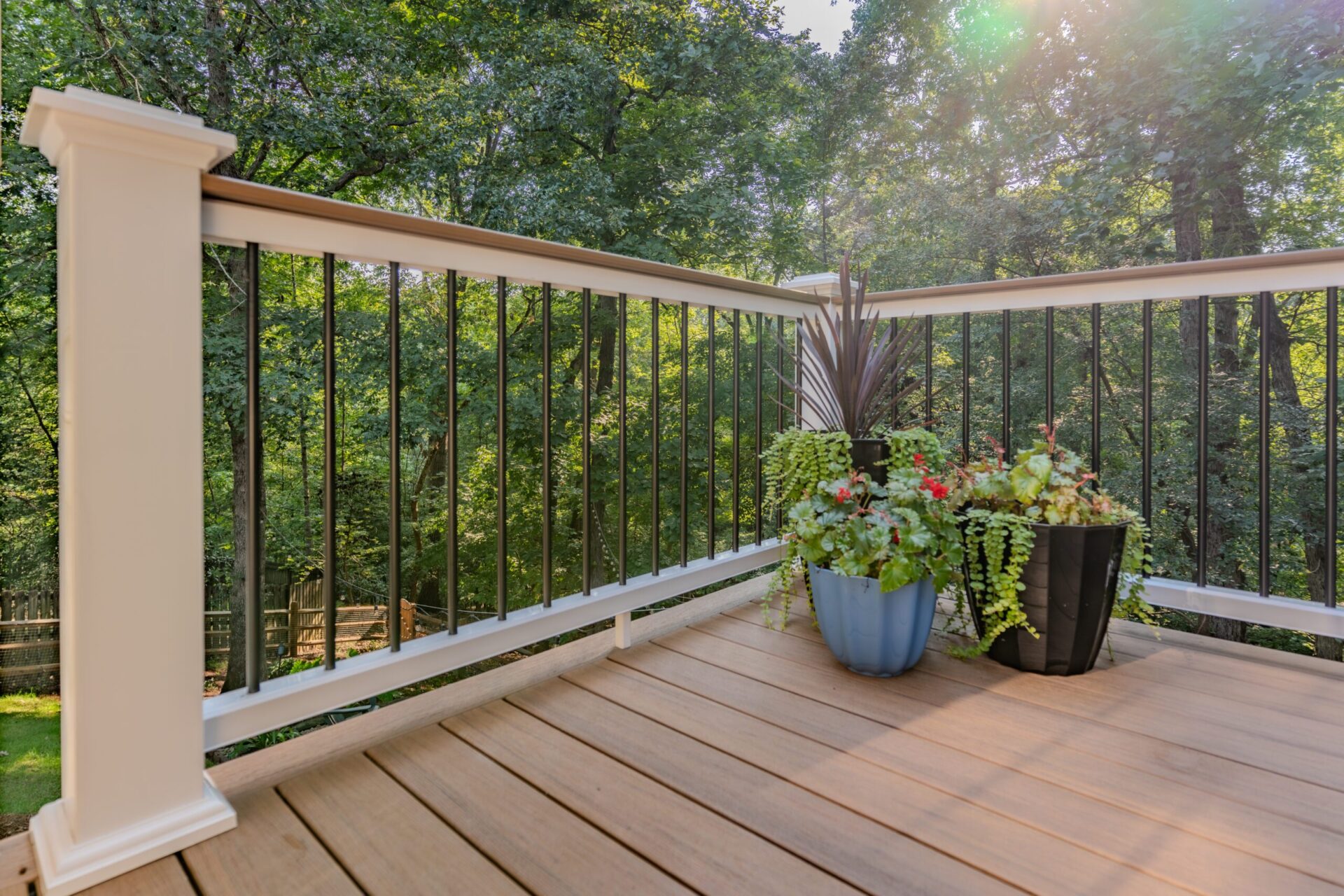 Close-up view of an elevated composite deck in Charlotte's Sardis Forest neighborhood, showcasing a white railing post with a tan TimberTech top rail, black metal balusters, and vibrant potted plants.