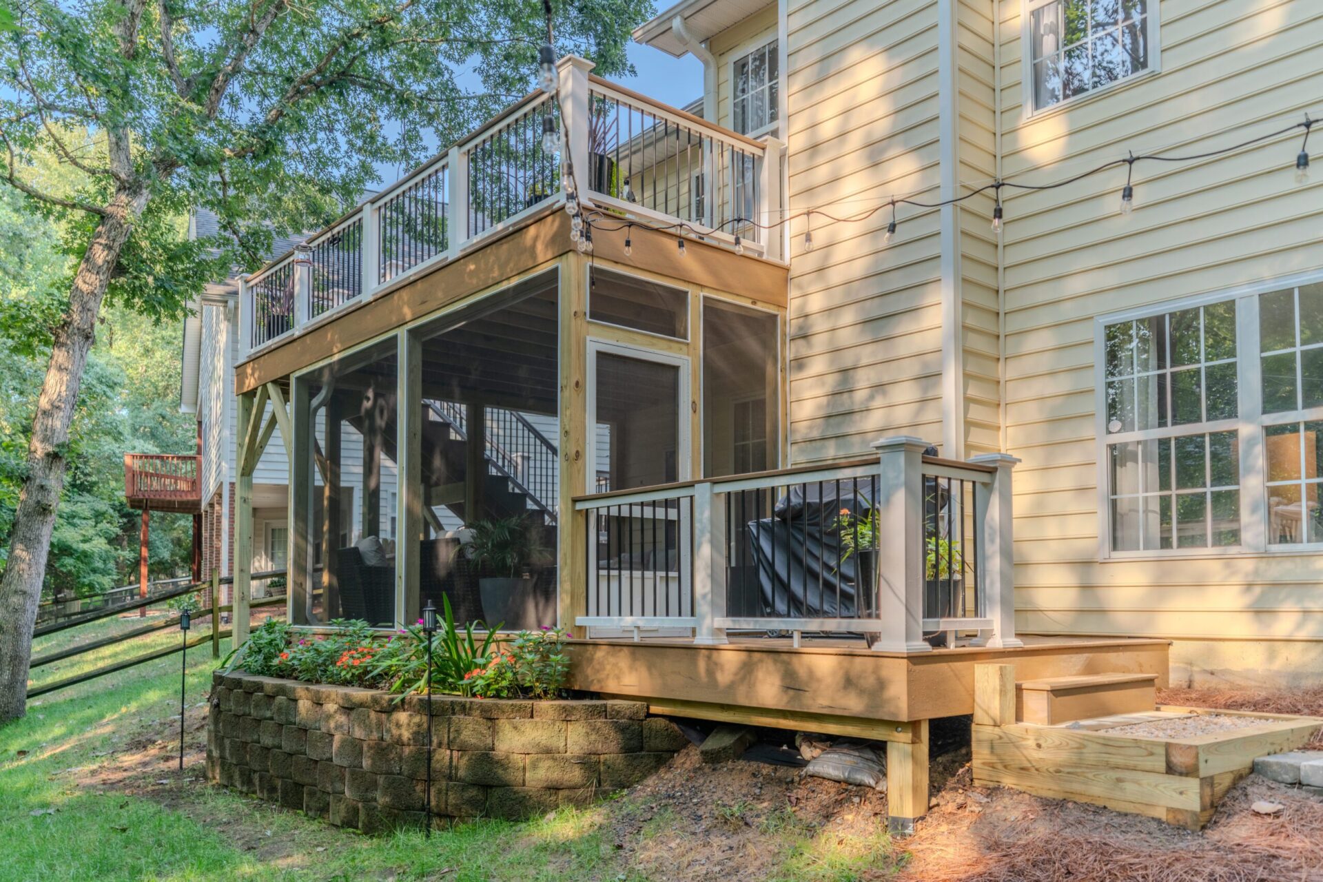 Exterior backyard view of a custom multi-level outdoor living space in Charlotte's Sardis Forest neighborhood, featuring an upper composite deck and lower screened-in porch built with TimberTech Antique Leather decking and matching railings with black balusters.