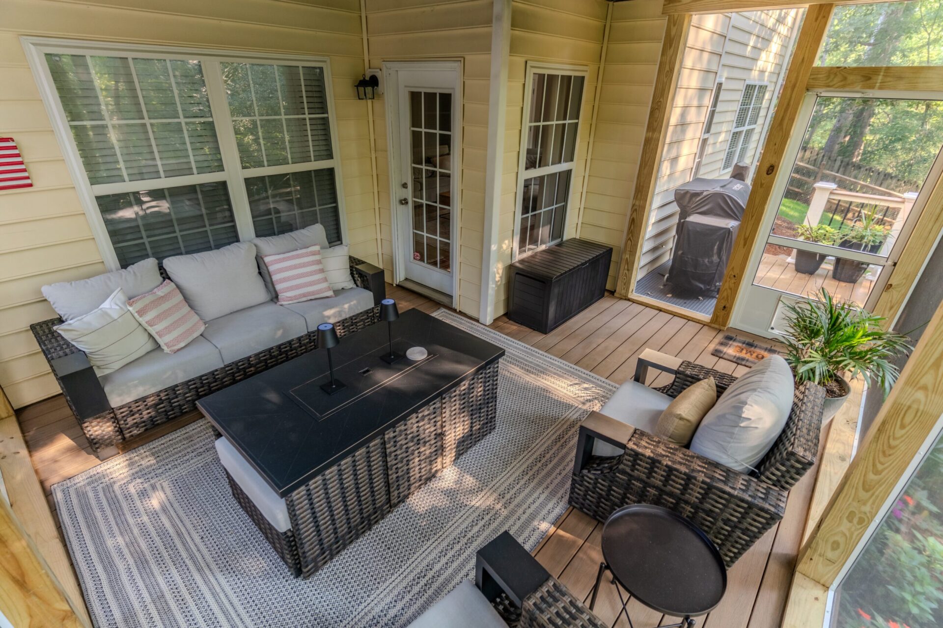Interior of a custom screened-in porch in Charlotte's Sardis Forest neighborhood, featuring TimberTech Antique Leather composite flooring, woven outdoor furniture, a large coffee table, and a patterned area rug.