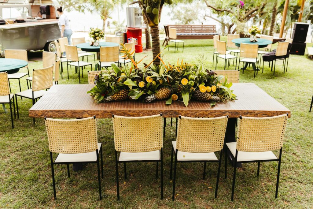 An outdoor party layout with a large wooden table, guest seating zones, and a food service area on a lawn.