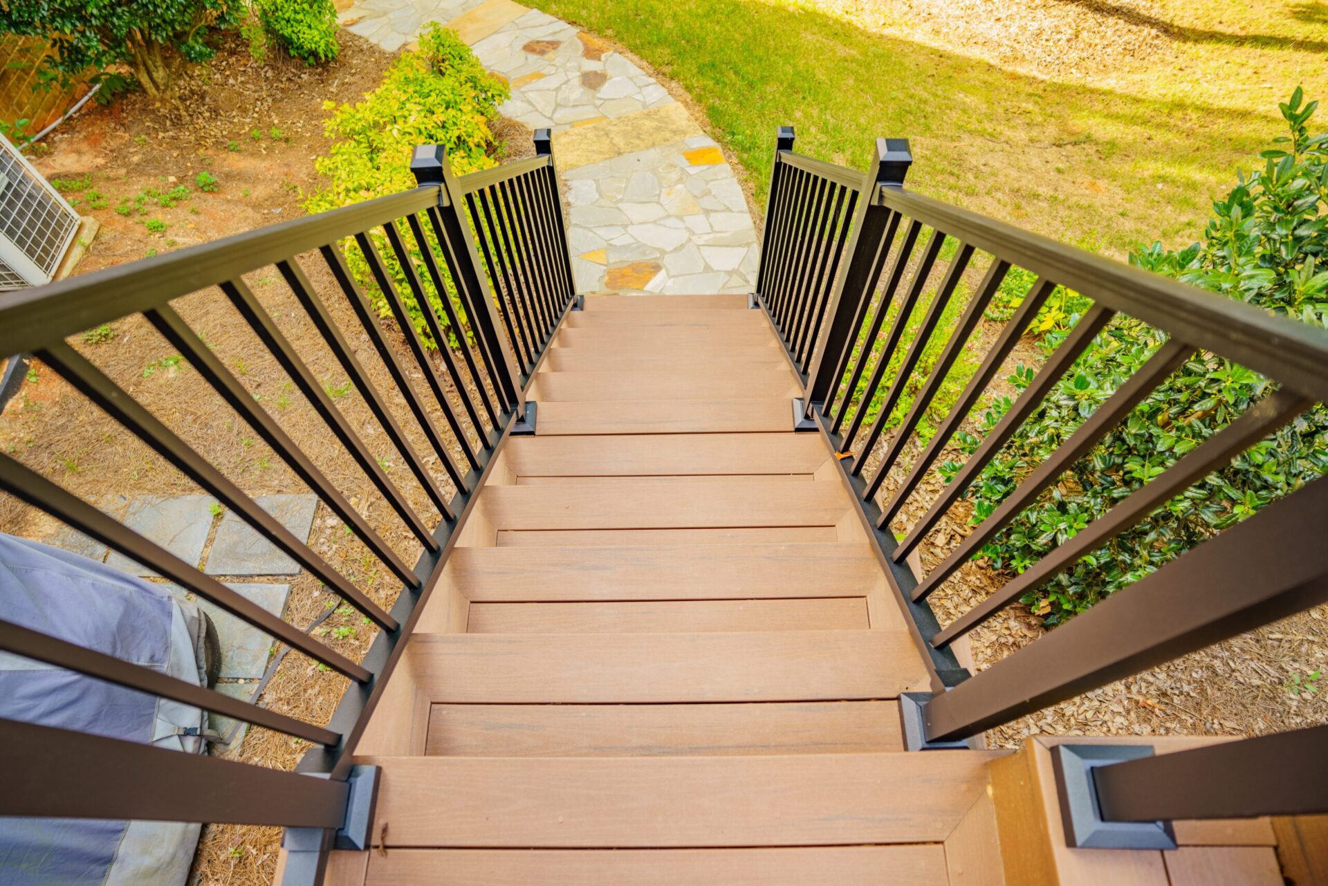 Brown composite deck stairs with black aluminum railings overlooking a stone walkway in Piper Glen, Charlotte.