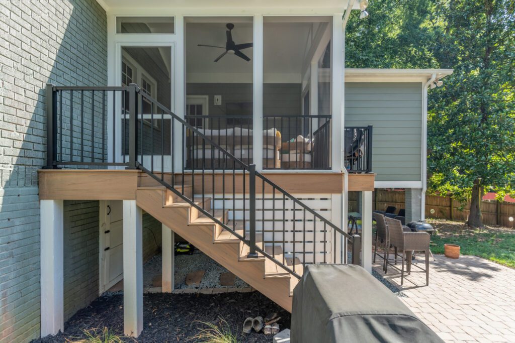 A backyard deck in Charlotte featuring black Trex aluminum railings on a staircase leading to a white screened-in porch.