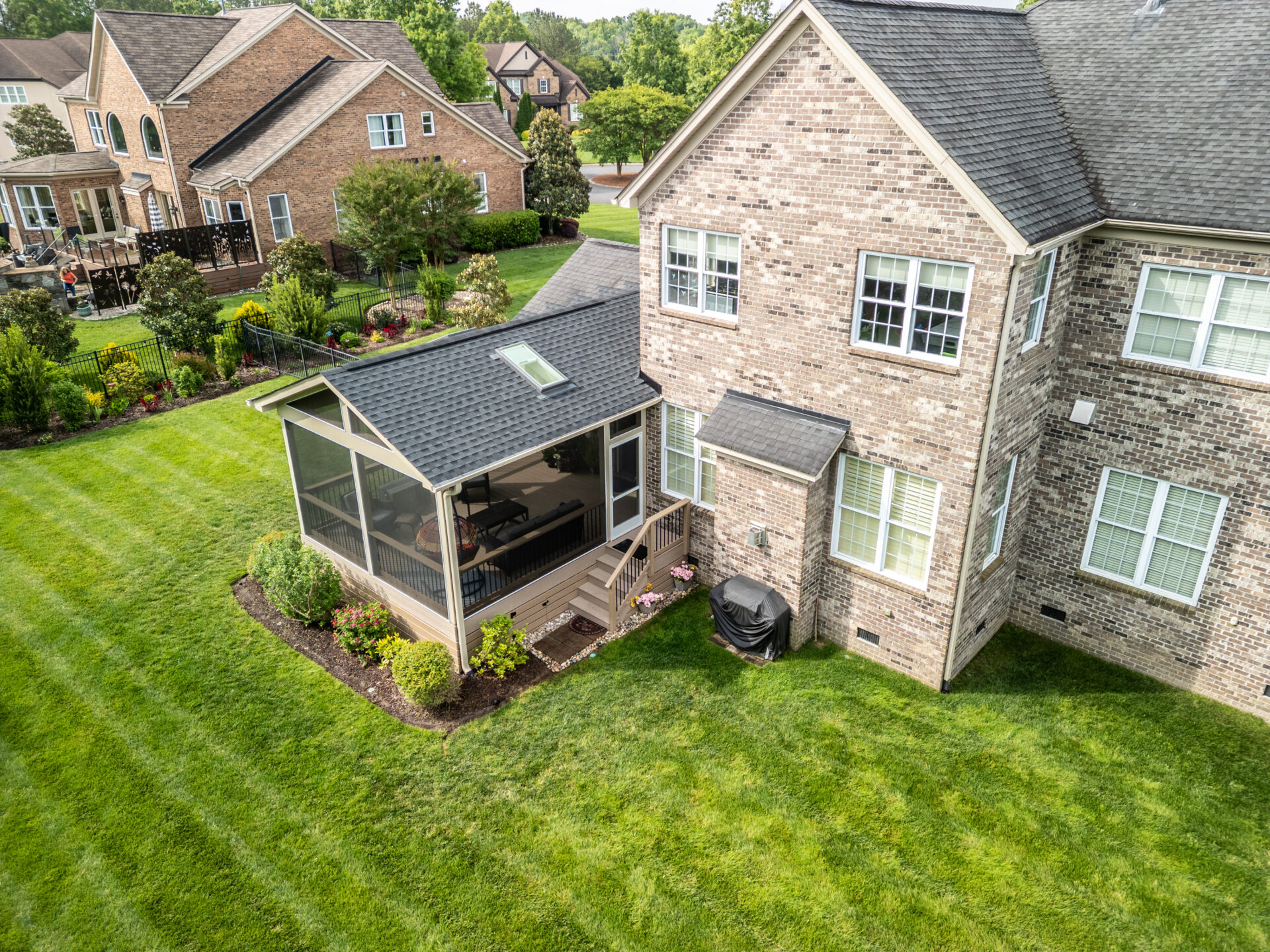 Aerial drone view of a custom deck-to-porch conversion on a brick home in Marvin Creek, Waxhaw. The new Screeneze screened porch features a gabled roof with a skylight, integrated Infratech heaters, and custom stairs leading to the lawn.