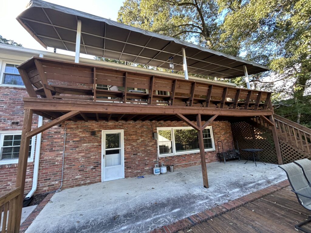 An aging, weathered wood deck staircase and railing on a brick house in Charlotte's Stonehaven neighborhood prior to a custom composite deck replacement.