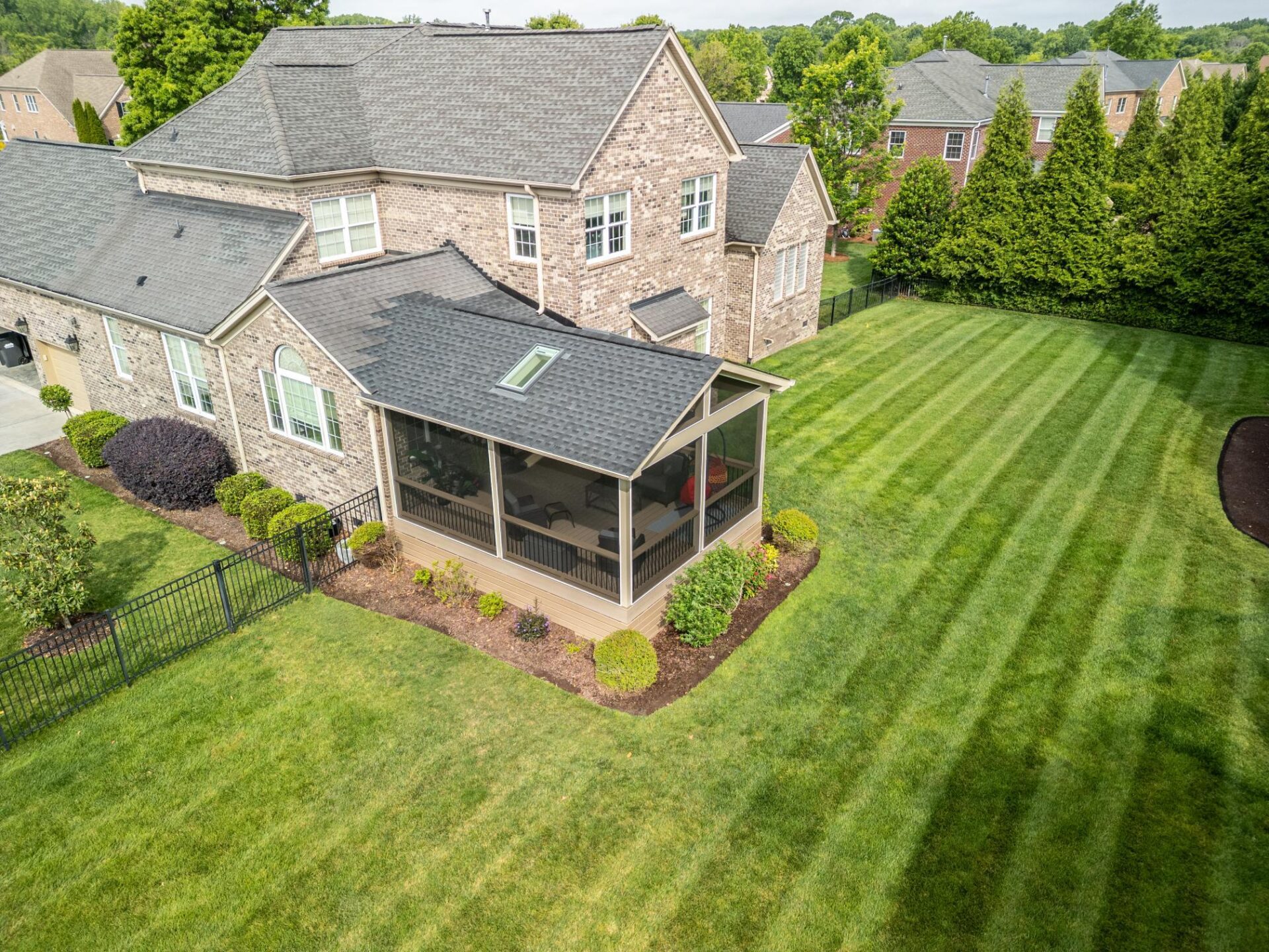 Aerial drone view of a completed custom screened porch conversion with an integrated architectural shingle roofline and skylight.