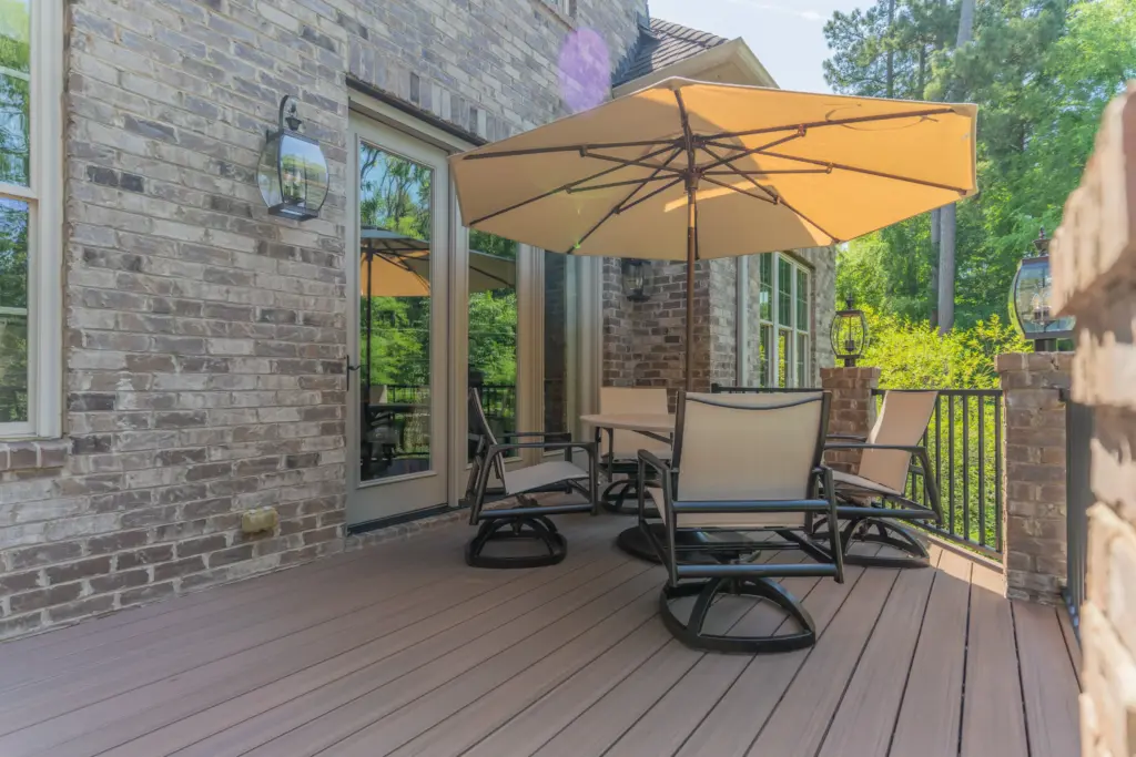 Close-up view of premium TimberTech Black Walnut composite decking boards installed on an elevated brick home's back deck with patio furniture and an umbrella.