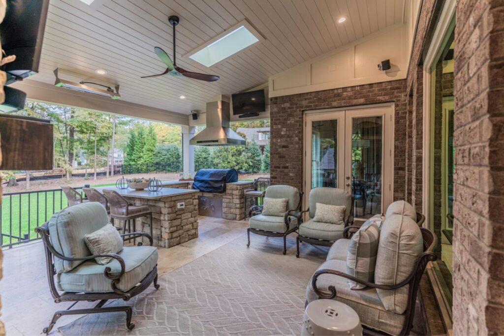 Custom outdoor kitchen and covered porch build in Mint Hill NC featuring a stacked stone island, skylights, outdoor fan, and patio seating.